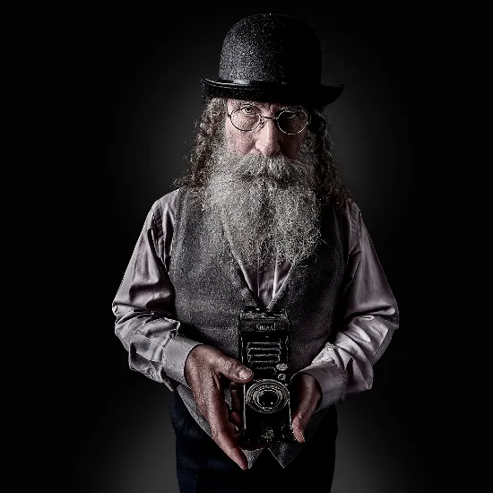 Foto de modelo con barba, lentes y cámara en las manos. Estilo vintage